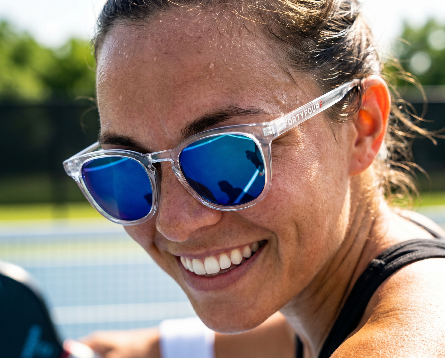 Player smiling courtside in FortyFour Shades with blue polarized lenses